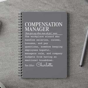 May include: A grey spiral-bound notebook featuring white text that defines a Compensation Manager as a workplace wizard who handles salaries, raises, bonuses, and pay questions, keeping employees hopeful and budgets from having an emotional breakdown.