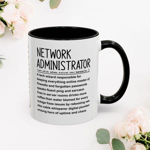 Könnte beinhalten: Eine weiße Keramiktasse mit schwarzem Innenraum und Henkel. Auf der Tasse steht in schwarzer Schrift "NETWORK ADMINISTRATOR" sowie eine humorvolle Definition. Die Tasse ist von weißen und rosa Blumen umgeben.