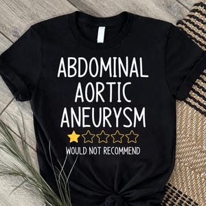 May include: Black t-shirt with white text: "ABDOMINAL AORTIC ANEURYSM" and a one-star rating. Below the rating is the text "WOULD NOT RECOMMEND". The shirt is made of a soft material.