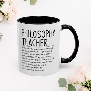 May include: A white ceramic mug with a black interior and handle. The mug displays the words "PHILOSOPHY TEACHER" in black, along with a definition. The mug is decorated with flowers.