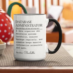 May include: White ceramic mug with a black handle and rim. The mug features the text "DATABASE ADMINISTRATOR" with a definition below. The text also includes "See Also: Charlotte".