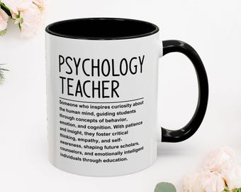 May include: A white ceramic Psychology Teacher mug with a black interior and handle. The mug features the text "PSYCHOLOGY TEACHER" and a definition of the profession. The mug is surrounded by pink flowers.