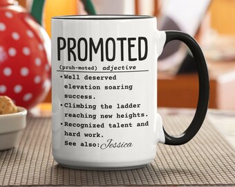 May include: White ceramic mug with a black rim and handle. The mug has black text that reads "PROMOTED (pruh-moted) adjective • Well deserved elevation soaring success. • Climbing the ladder reaching new heights. • Recognized talent and hard work. See also: Jessica"
