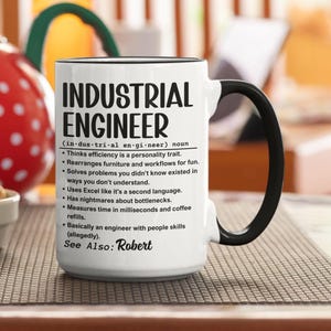 Może przedstawiać: Biały ceramiczny kubek z czarnym uchwytem i obramowaniem. Kubek zawiera tekst "INDUSTRIAL ENGINEER" z definicją i humorystycznymi punktami dotyczącymi zawodu. Imię "Robert" jest również uwzględnione.