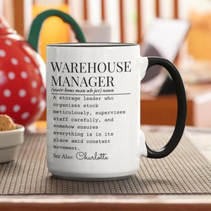 Könnte beinhalten: Weißer Keramikbecher mit schwarzem Henkel und Rand. Der Becher zeigt den Text "WAREHOUSE MANAGER" und eine Definition, mit dem Namen "Charlotte" unten. Ein perfektes Geschenk für einen Lagerleiter.