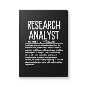 May include: Black and white notebook with the text "RESEARCH ANALYST noun(n.) Jessica" and a definition of the term. The definition describes a research analyst as a person who dives into data, armed with logic, in search of insights.