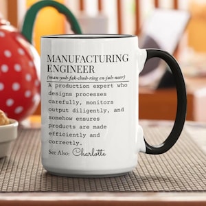Puede incluir: Una taza de cerámica blanca con asa y borde negros, con texto impreso en negro que define a un ingeniero de fabricación como un experto en producción que diseña procesos, supervisa la producción y garantiza la eficiencia. Incluye el texto See Also: Charlotte.