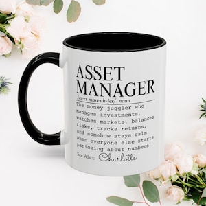 May include: A white ceramic mug with a black handle and interior rim. The front features black text defining an asset manager as a money juggler who manages investments, watches markets, balances risks, tracks returns, and stays calm. See Also: Charlotte.