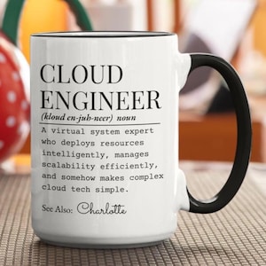 Könnte beinhalten: Ein weißer Keramikbecher mit schwarzem Henkel und schwarzem Innenrand. Auf der Vorderseite steht in schwarzer Schrift die Definition eines Cloud-Ingenieurs als Experte für virtuelle Systeme, der Ressourcen intelligent verwaltet und Cloud-Technik vereinfacht. Siehe auch: Charlotte.