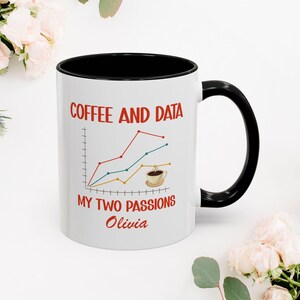 Könnte beinhalten: Weißer Keramikbecher mit schwarzem Innenraum und Henkel. Der Becher zeigt den Text "COFFEE AND DATA" in Rot, zusammen mit einem Diagramm und einer Kaffeetassen-Illustration. Darunter steht "MY TWO PASSIONS Olivia".