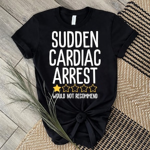 Puede incluir: Camiseta negra con texto blanco que dice "Paro cardíaco repentino" y una calificación de una estrella que dice "No lo recomiendo".