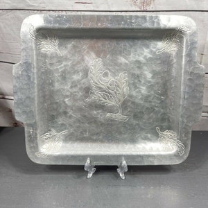 May include: A silver metal serving tray with an embossed design of oak leaves and acorns. The tray has a hammered finish and rounded corners.