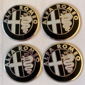May include: Four black and silver Alfa Romeo car emblems with the words "Alfa Romeo" written in a silver circle around the logo. The logo features a white cross and a white snake.