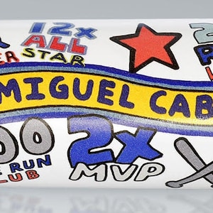 May include: A white baseball bat with a blue and red design. The bat features the number 24, the name "Miguel Cabrera", and the text "2003 Champ", "2012 Triple Crown", "Detroit", "500 Home Run Club", "2x MVP", "3000 Hit", and "24 2009-2023".