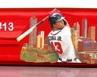 May include: A red baseball bat with a limited edition inscription, "Limited Edition 12 of 100", and a player's name, "Ronald Acuña Jr #13". The bat features a graphic of the player in action, along with the text "2023 Season" and "First player in history with 20+ HR 40+ SB 50+ RBI before the All-Star Break".