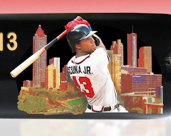 May include: A black baseball bat with gold lettering and a color image of a baseball player. The bat is a limited edition, officially licensed product. Text includes "RONALD ACUÑA JR #13" and "2023 SEASON".