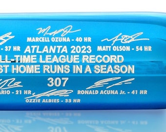 May include: A blue and red baseball bat with the text "PLAYERS" and "ATLANTA 2023 ALL-TIME LEAGUE RECORD MOST HOME RUNS IN A SEASON 307" on it. The bat is signed by various players.