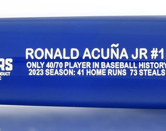 May include: A blue baseball bat with a white inscription that reads "Ronald Acuña Jr. #13 Only 40/70 Player in Baseball History 2023 Season: 41 Home Runs 73 Steals" and a white logo that reads "The Players Officially Licensed Product of MLB Players, Inc.". The bat is a limited edition, 23 of 500. The bat has a picture of Ronald Acuña Jr. swinging a bat.