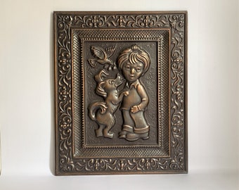 May include: A framed metal wall art piece depicting a boy and a dog. The boy is wearing a shirt and pants, and the dog is standing on its hind legs. The piece is in a brown metal frame with an ornate design.