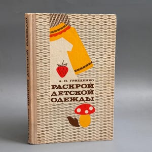 May include: A hardcover book with a beige textured cover featuring a yellow garment illustration, a red strawberry, and a red mushroom. The text on the cover reads A. P. GRISHCHENKO RASKROY DETSKOY ODEZHDY in brown, with matching text on the spine.