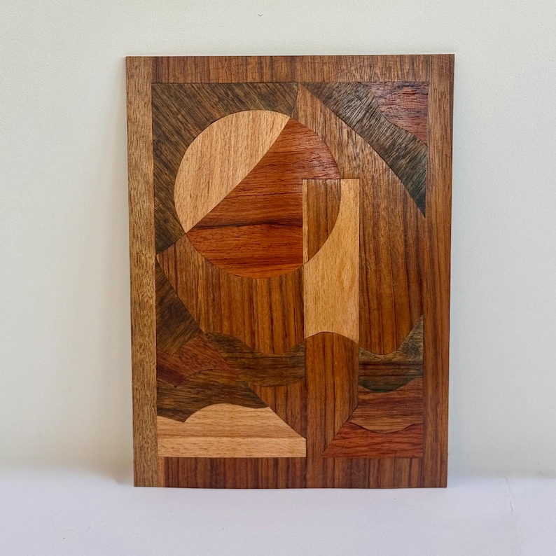 Peut inclure: &OElig;uvre d'art g&eacute;om&eacute;trique en bois avec un cercle en forme de soleil et des formes triangulaires dans des tons de marron, de rouge et de beige. L'&oelig;uvre rectangulaire a une bordure marron fonc&eacute;.