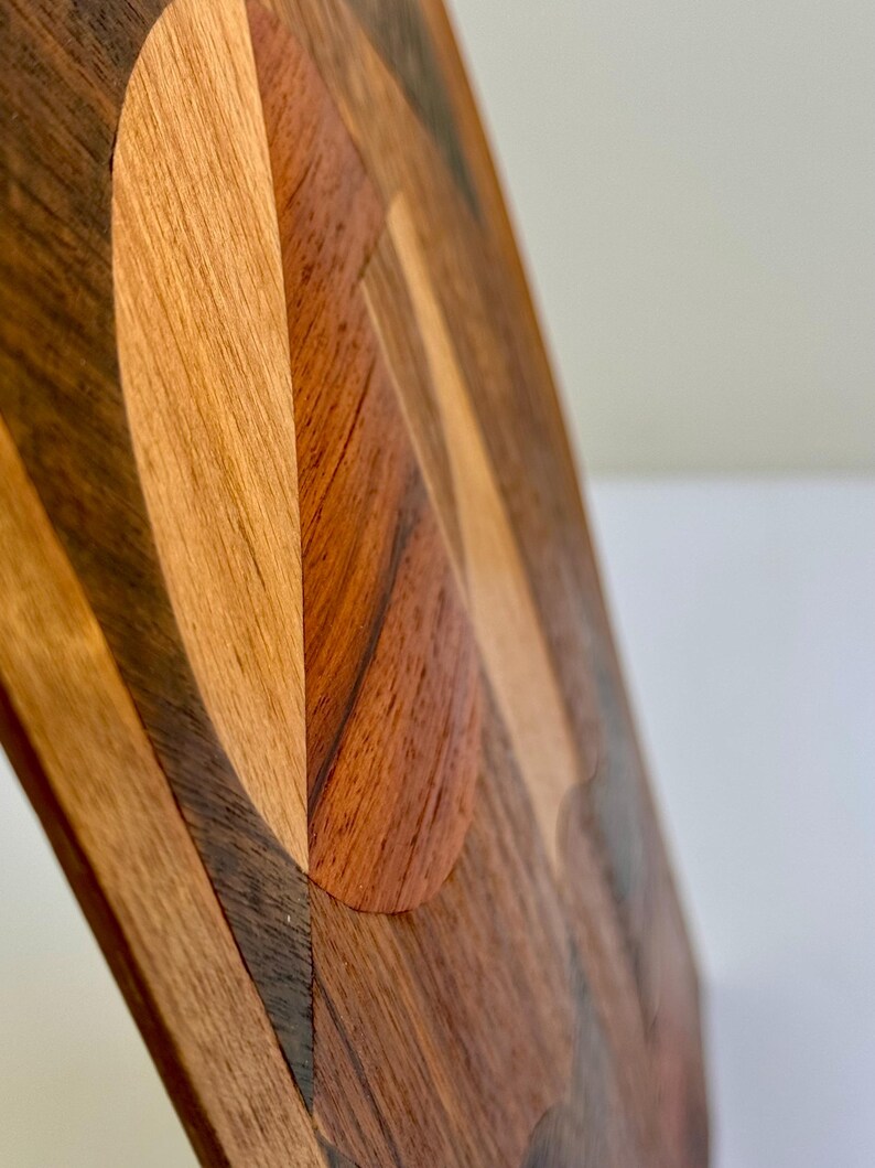 Peut inclure: Gros plan sur un objet d&eacute;coratif en bois avec un design g&eacute;om&eacute;trique. L'objet pr&eacute;sente une vari&eacute;t&eacute; de tons de bois, notamment brun clair, brun fonc&eacute; et brun rouge&acirc;tre, dispos&eacute;s en motif de mosa&iuml;que. Le design comprend des formes courbes et angulaires.