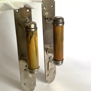Puede incluir: Dos manijas de puerta antiguas con acabado metálico cepillado. Las manijas tienen empuñaduras cilíndricas con un patrón marrón claro y amarillo. Las manijas son para puertas interiores.