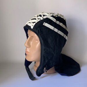Puede incluir: Un gorro de lana negro con un diseño de encaje blanco y una solapa de cuello de lana negra. El gorro tiene un anillo de metal en el lateral.