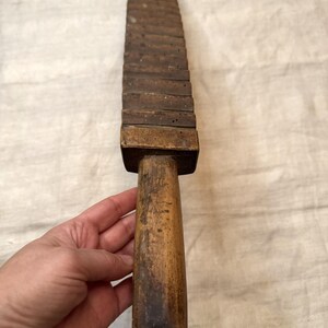 Pu&ograve; includere: Un lungo attrezzo di legno con un manico e una serie di blocchi rettangolari impilati. L'attrezzo &egrave; in legno marrone scuro e ha un aspetto usurato e rustico.