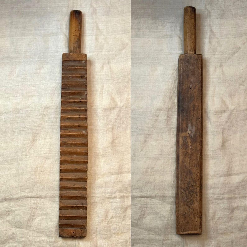 Pu&ograve; includere: Un lavandino in legno con un manico a un'estremit&agrave;. Il lavandino ha una serie di creste su un lato e una superficie liscia sull'altro.