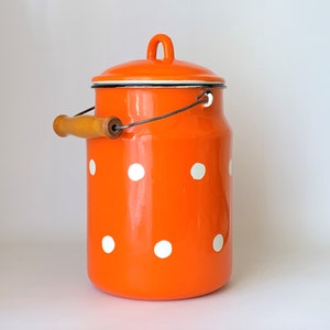 May include: Orange enamelware milk can with a white polka dot pattern and a wooden handle. The can has a lid.