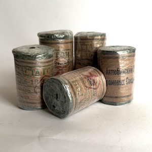 May include: Five spools of twine wrapped in green plastic. The spools are labeled in Cyrillic script with the text "Актюбинский Домовый Союз".
