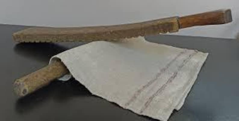 Pu&ograve; includere: Due palette di legno con manico marrone e una lama lunga e piatta. Le lame hanno un bordo seghettato. Le palette sono incrociate su un panno di lino bianco.
