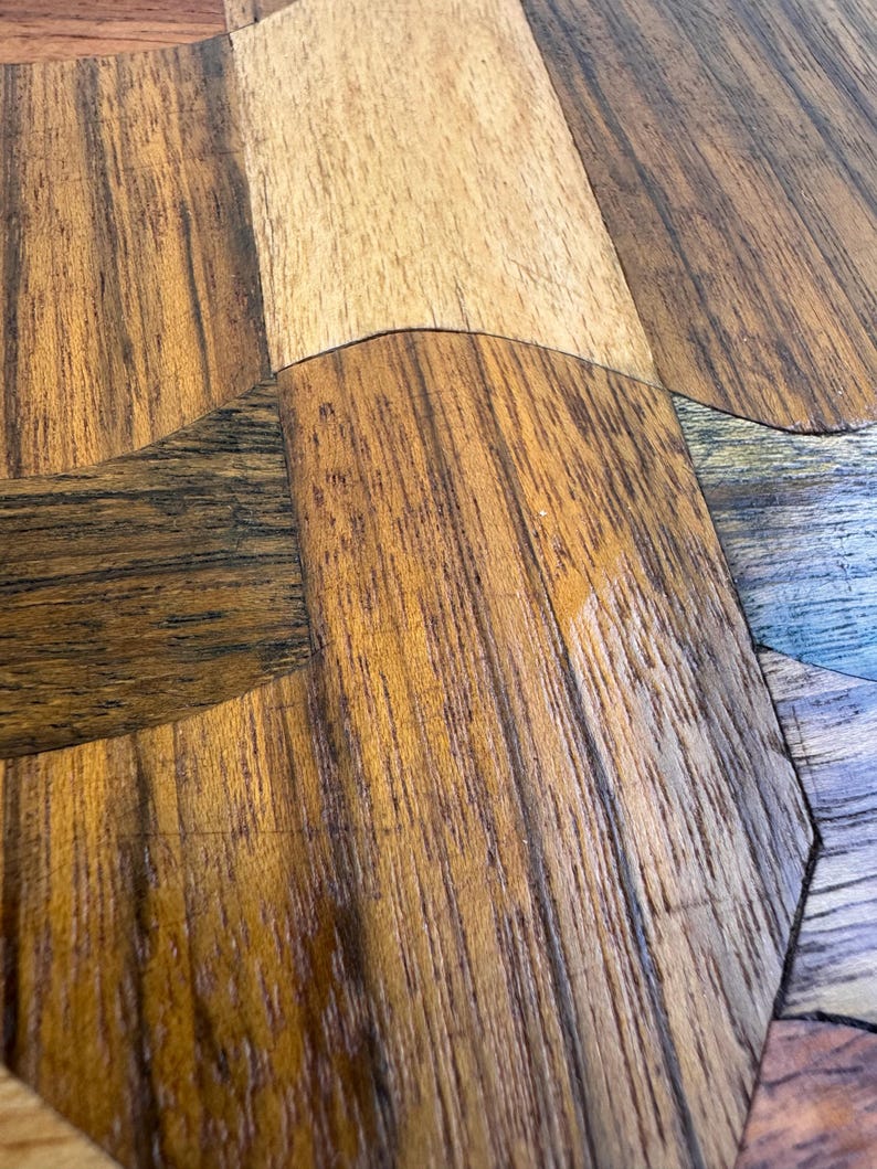 Peut inclure: Gros plan sur une surface en bois avec un motif g&eacute;om&eacute;trique. Le bois pr&eacute;sente une vari&eacute;t&eacute; de tons chauds, dont le beige clair, le marron moyen et le marron fonc&eacute;, dispos&eacute;s dans un motif en mosa&iuml;que. Le grain du bois est visible.
