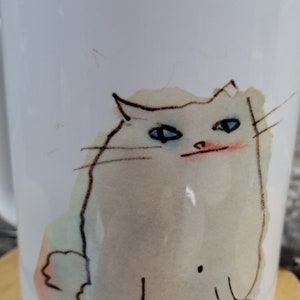 Puede incluir: Taza de cerámica blanca con una ilustración de acuarela de un gato blanco con ojos azules. El gato está sentado con la cola enroscada detrás de él.