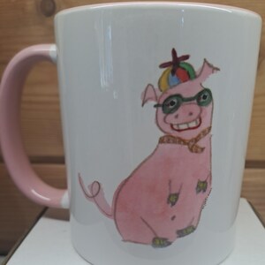 May include: White ceramic mug with a pink handle and rim. The mug features a whimsical illustration of a pink pig wearing glasses, a hat, and a scarf. The pig is smiling. The mug is designed for beverages.