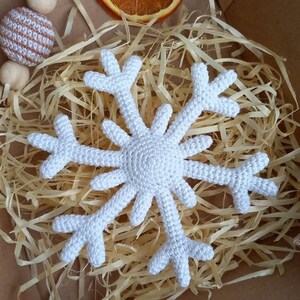 May include: A white crocheted snowflake ornament in a box with shredded paper. The snowflake is a popular Christmas decoration.