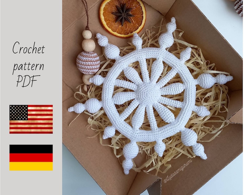 May include: A white crochet snowflake ornament with a detailed design, displayed in a cardboard box with straw. The image includes text that reads "Crochet pattern PDF" and flags of the USA and Germany.