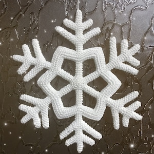 May include: A white, crocheted snowflake ornament, suspended by a thin white string. The snowflake has a six-sided symmetrical design with intricate detailing. The background is a textured, dark surface with sparkling accents.