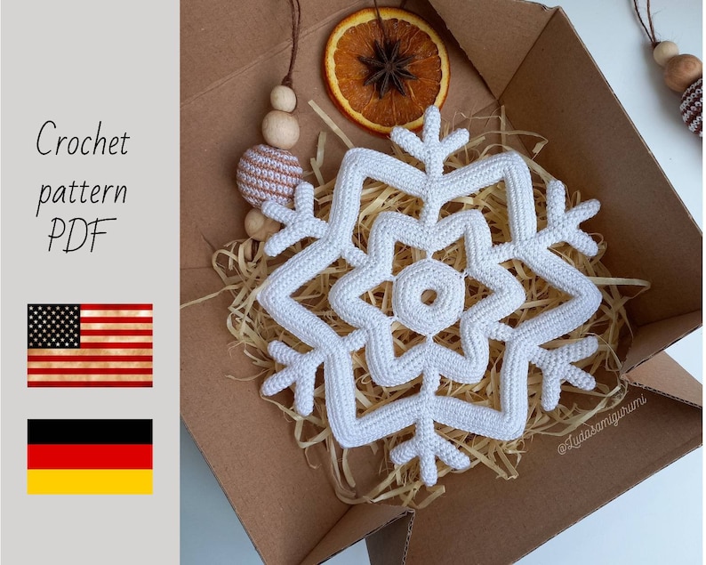 May include: A white crochet snowflake, displayed in a cardboard box with dried orange slices and decorative wooden beads. The text "Crochet pattern PDF" is visible, along with the American and German flags.