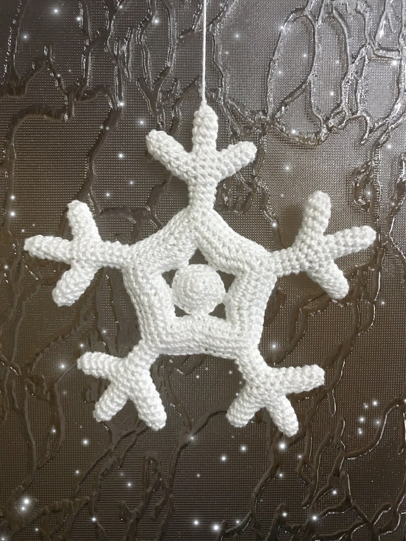 May include: A white, crocheted snowflake ornament with six symmetrical arms and a central sphere. The snowflake is suspended by a thin white string, perfect for holiday decor. The background is a textured, dark surface with sparkling accents.