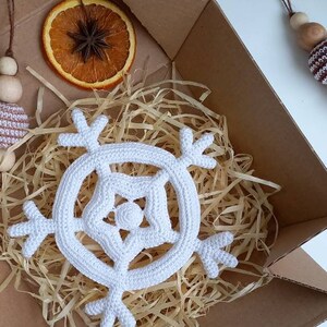 May include: A white crocheted snowflake ornament in a cardboard box with shredded paper.