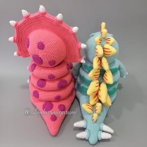 May include: Two crocheted dinosaur toys, one pink with purple spots and a frill, the other blue with yellow stripes and a spiky back.  @Ludasamigurumi