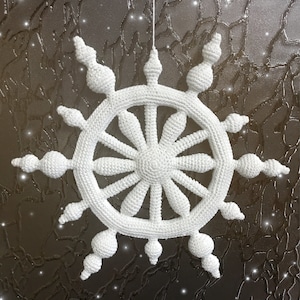 May include: A white, crocheted snowflake ornament. The snowflake is suspended by a white string and features a circular design with radiating spokes and decorative, rounded elements. The background is a textured, dark surface.
