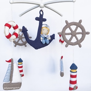 May include: A nautical themed baby mobile with a crocheted anchor, a sailor doll, a life preserver, a ship's wheel, and two lighthouses.