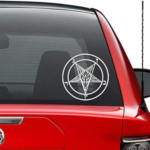 May include: A white vinyl sticker of a pentagram with a goat's head inside. The pentagram is surrounded by a circle with Hebrew characters. The sticker is on the back window of a red car.