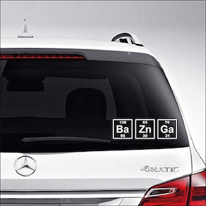 May include: White car with a periodic table sticker on the rear window. The sticker features the chemical symbols Ba, Zn, and Ga, with their atomic numbers and weights. The car has a Mercedes-Benz logo.