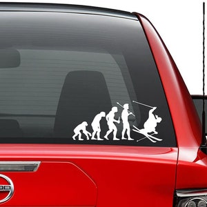 May include: A white vinyl sticker depicting the evolution of man, ending with a skier in a white silhouette. The skier is in mid-air, with skis and poles, and is wearing a helmet. The sticker is on a red car window.