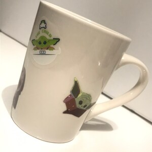 Puede incluir: Taza de cer&aacute;mica blanca con un personaje verde de la franquicia Star Wars, "The Child", en ella. El personaje se representa en dos poses diferentes. La taza tiene un asa.