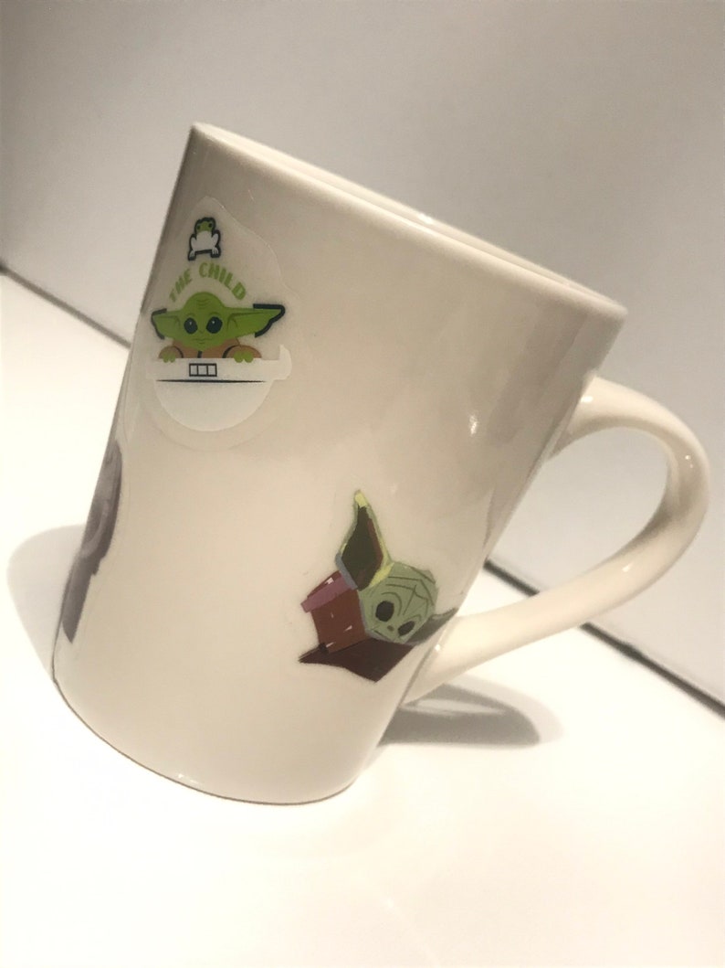 Puede incluir: Taza de cer&aacute;mica blanca con un personaje verde de la franquicia Star Wars, "The Child", en ella. El personaje se representa en dos poses diferentes. La taza tiene un asa.